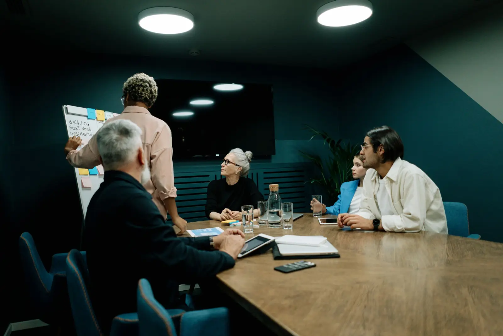 A board meeting in a dark-walled room.