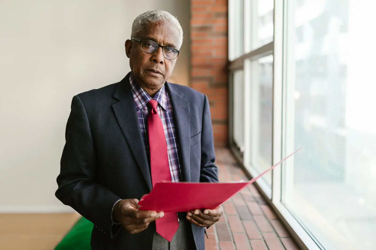 A senior leader holding a red folder by a window.