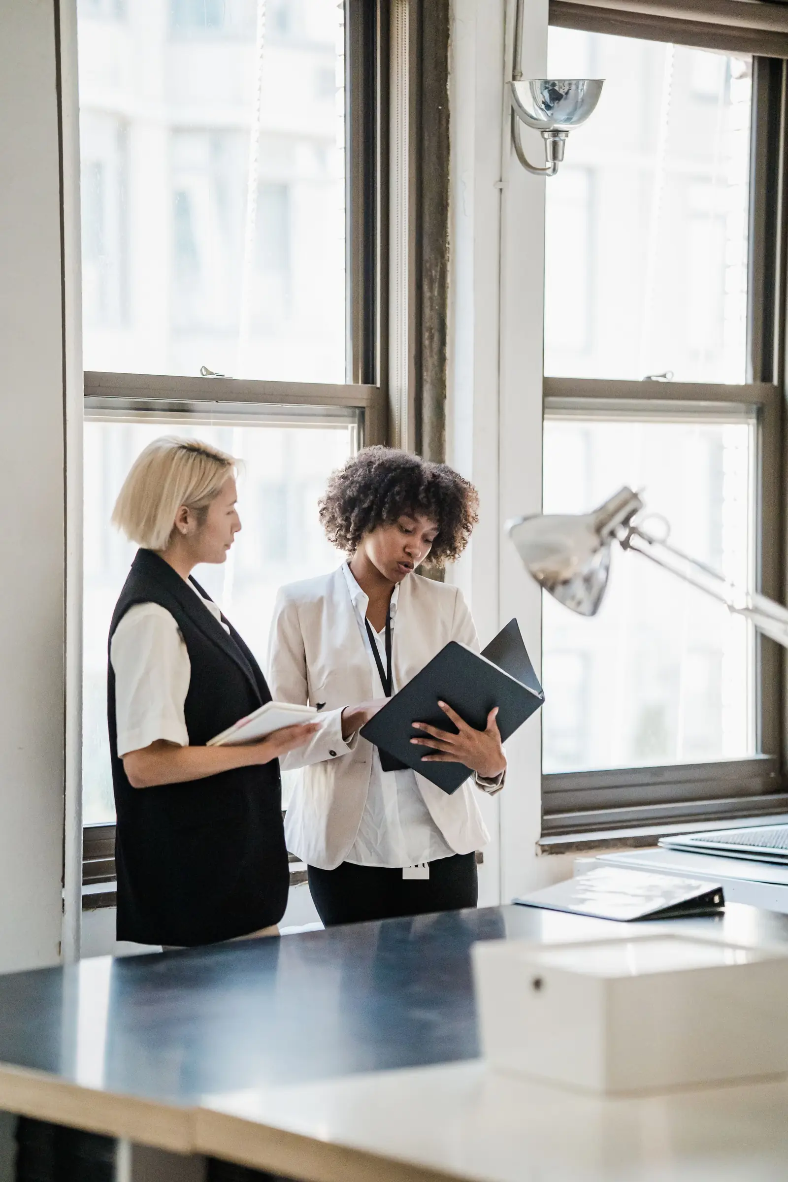 Two colleagues reviewing a document together by an office window.